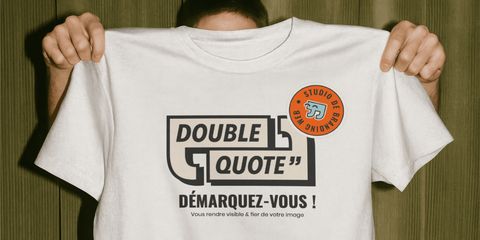 Personne tenant un t-shirt blanc Double Quote, avec le logo, l'accroche « Démarquez-vous ! » et un badge rond orange.